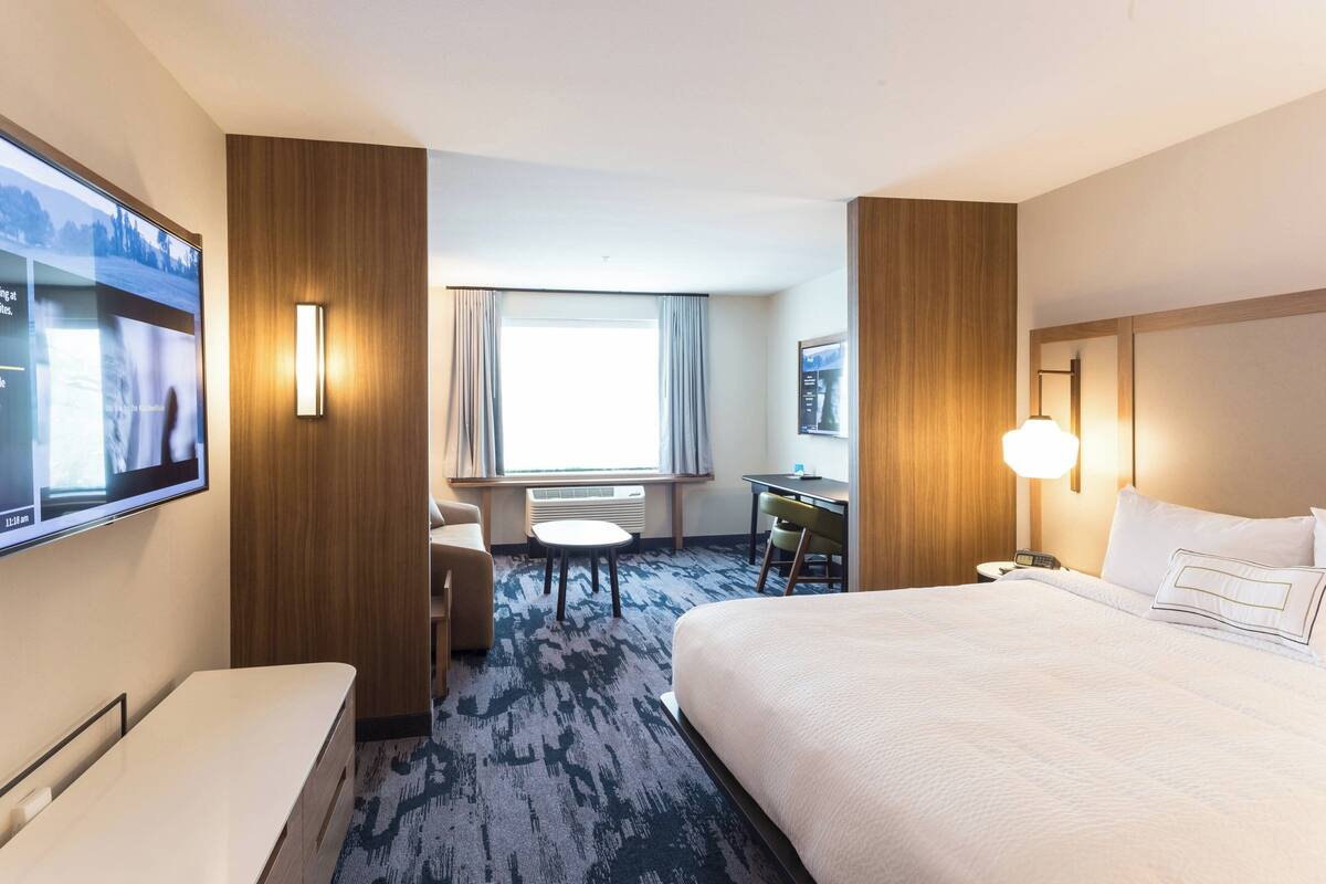 A hotel room with a large bed, a desk, a chair, a TV, and a window with curtains.