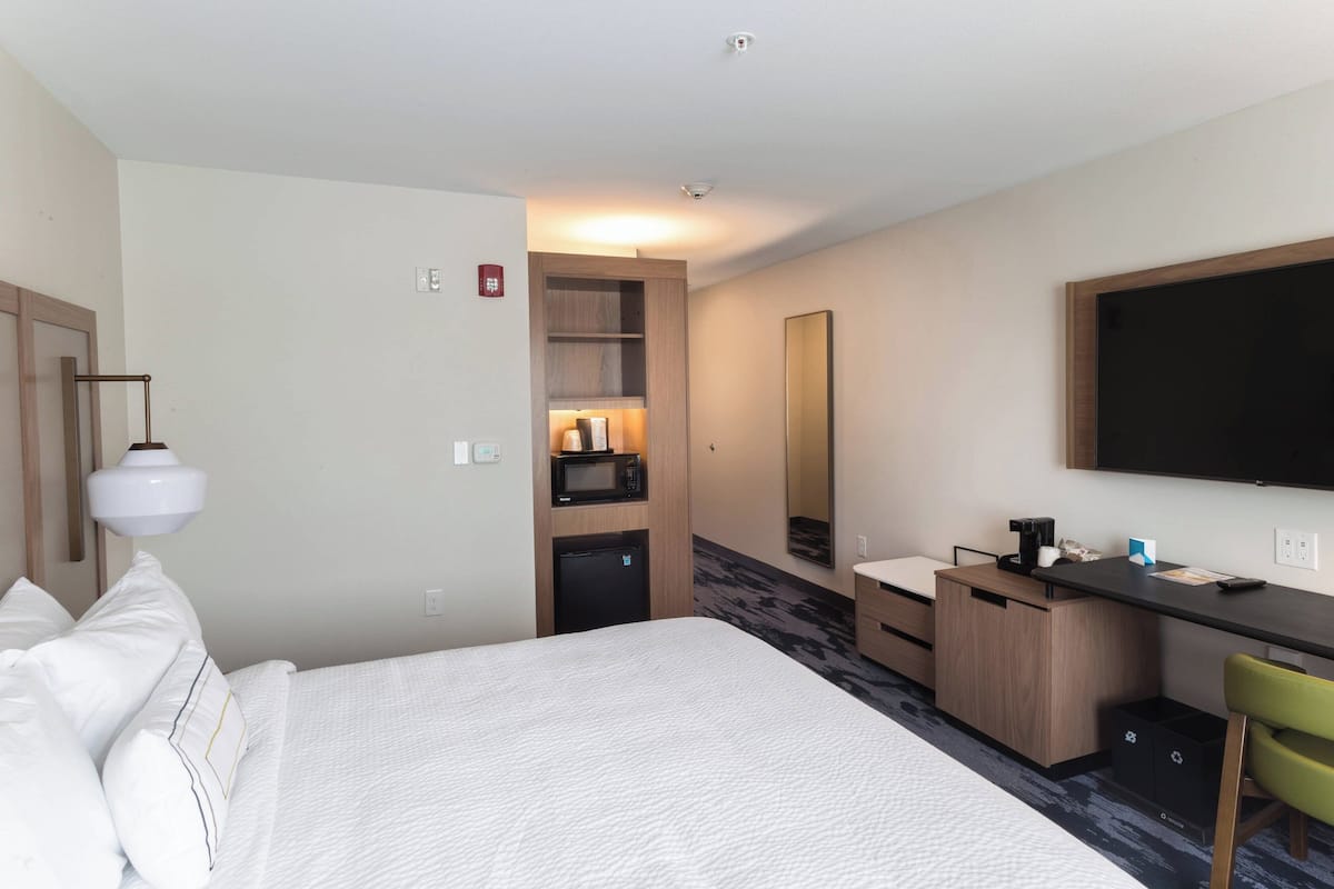 A hotel room with a bed, a desk, a microwave, a refrigerator, a mirror, and a television.