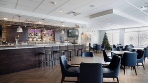 Un restaurante moderno con zona de bar, suelo de madera y un ventanal que ofrece vistas al exterior.