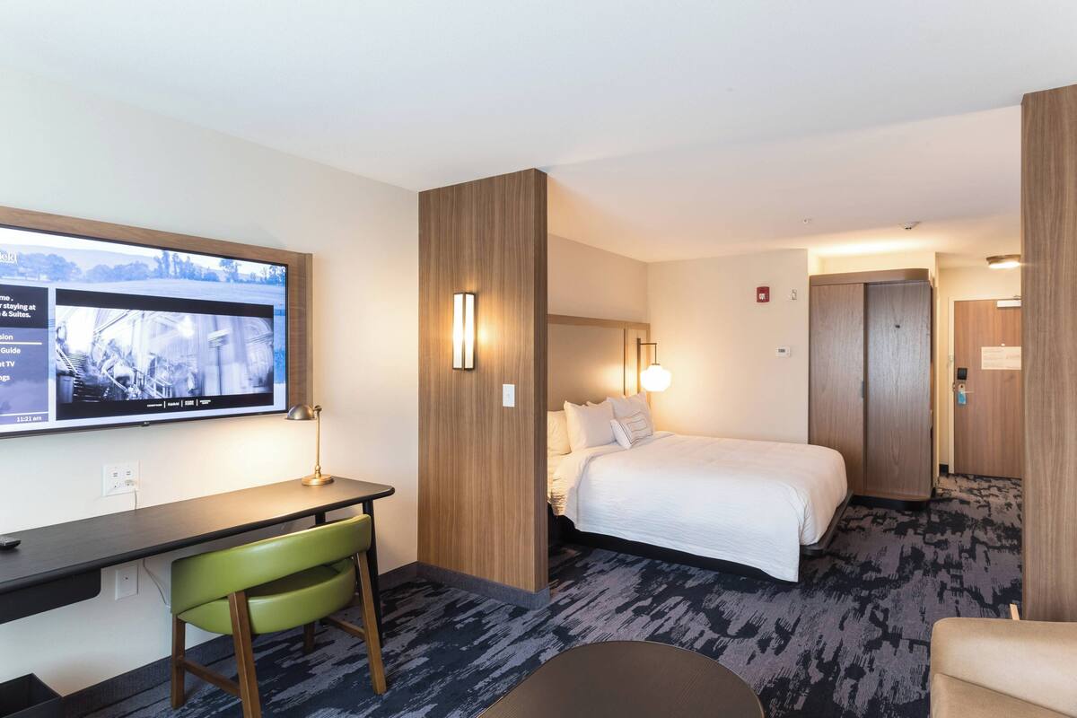 A hotel room with a bed, desk, chair, TV, and a wardrobe.