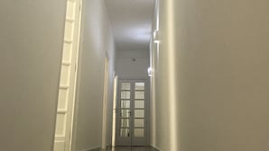 Un long couloir étroit, doté d’un sol ciré, de murs blancs et d’une porte au fond.