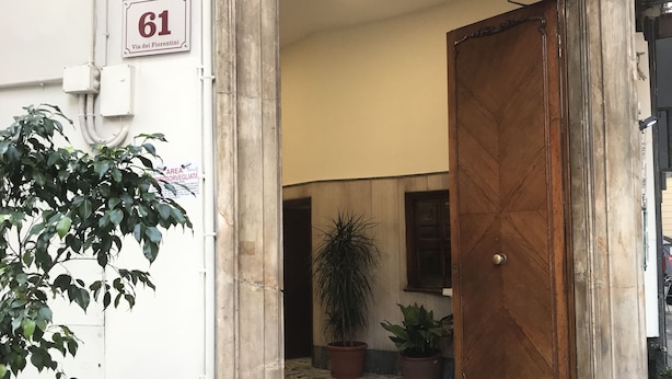 Une entrée d’immeuble avec une plaque numérotée, une porte en bois et des plantes en pot.