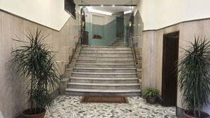 Un escalier menant à un palier dont le sol est recouvert de carreaux et où l’on trouve, de part et d’autre, des plantes en pot.