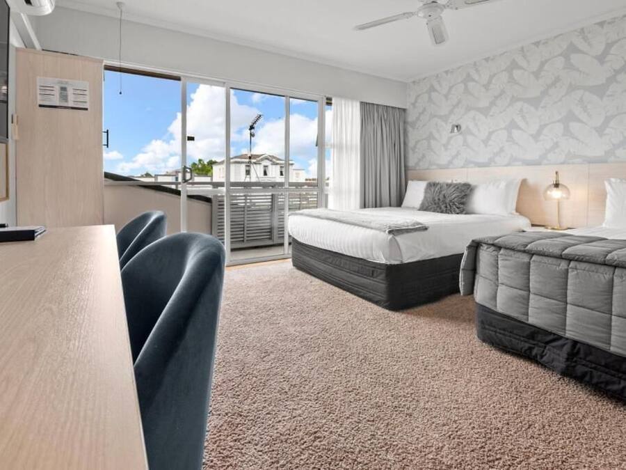 A hotel room with a bed, a desk, and a chair. There is a window with a view of buildings outside.
