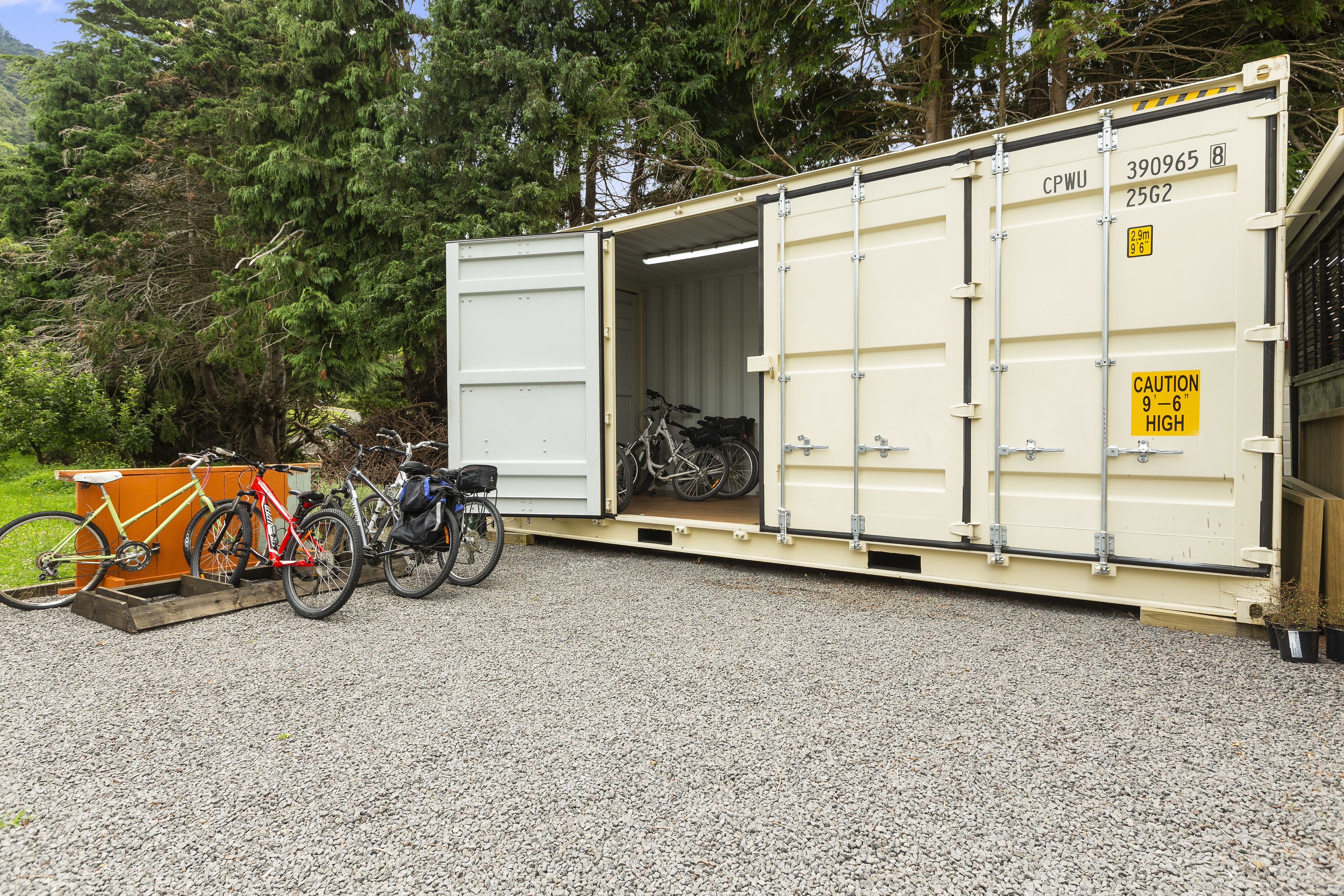 A large container with bicycles inside, parked on a gravel surface with trees in the background.
