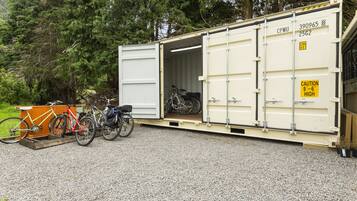 A large container with bicycles inside, parked on a gravel surface with trees in the background.