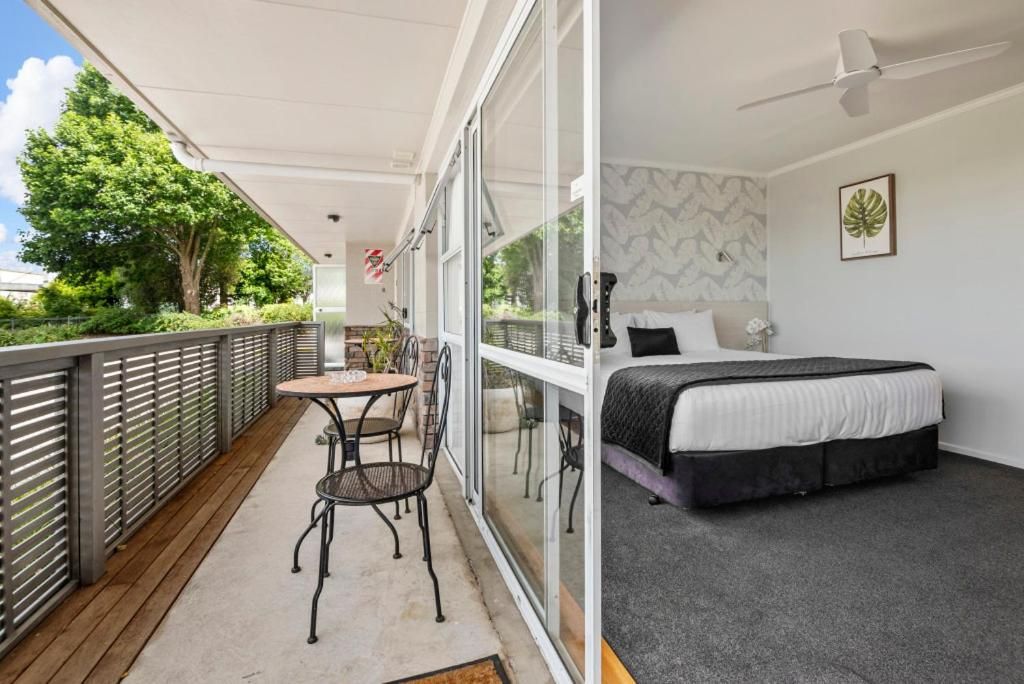 A balcony with a table and chairs, a bed with a black headboard, and a window with a leaf pattern.
