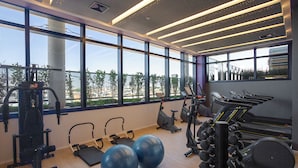 Een sportschool met diverse fitnessapparaten, grote ramen en uitzicht op de stad.