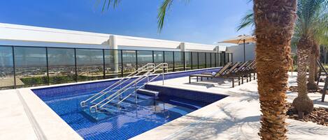 Una piscina en la azotea con agua cristalina, barandilla de vidrio y palmeras.