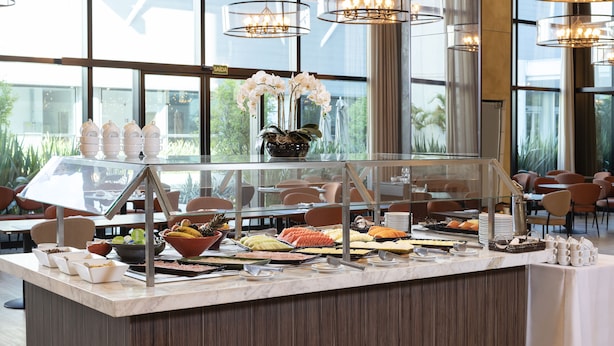Een buffetgedeelte met diverse gerechten en een glazen display, gelegen in een ruimte met grote ramen en moderne verlichting.