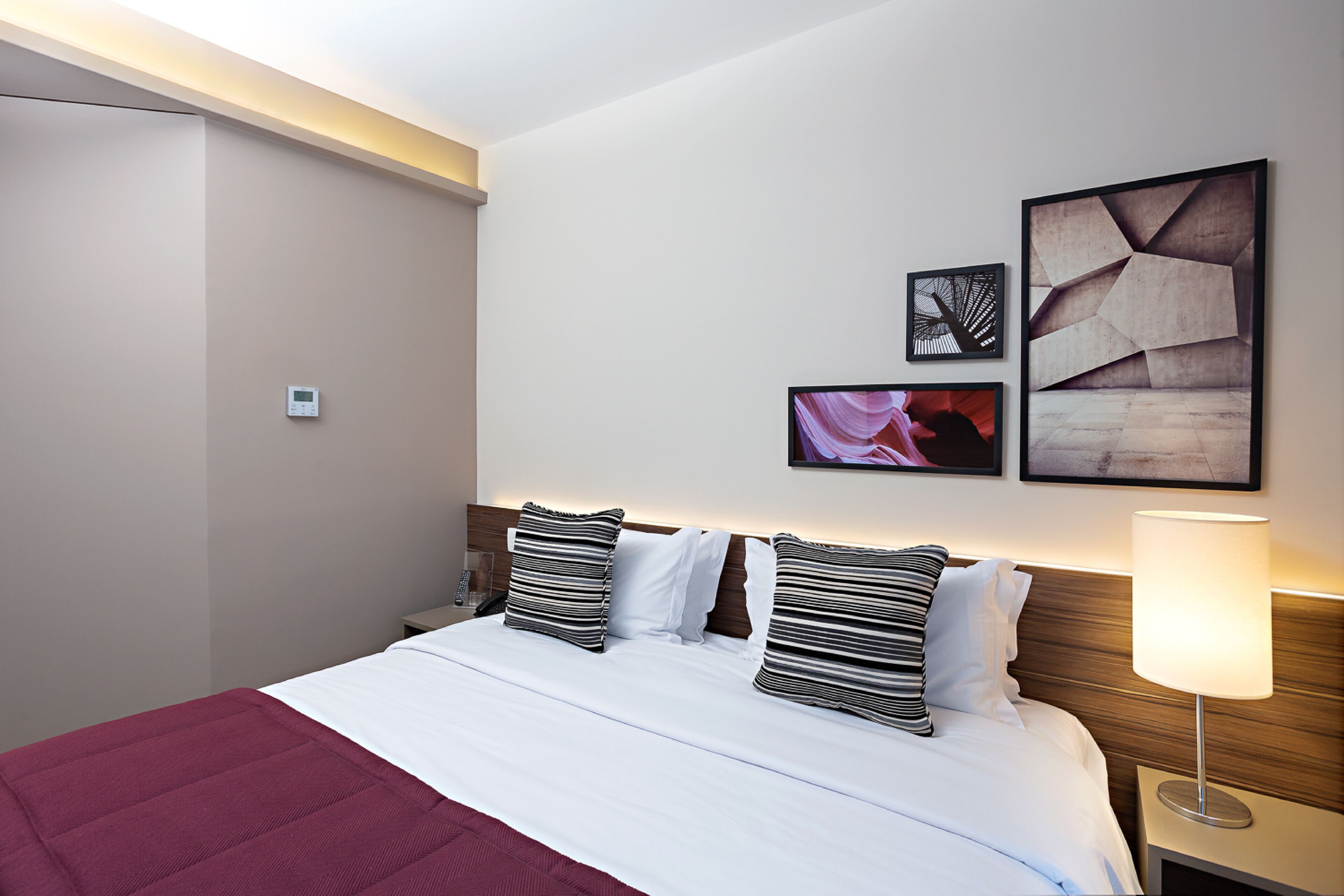 A hotel room with a bed, a nightstand, a lamp, and wall art.