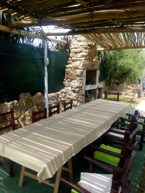 An outdoor dining area with a long table and chairs, a stone wall, and a grill. - Hosteria San Benito (Concordia)