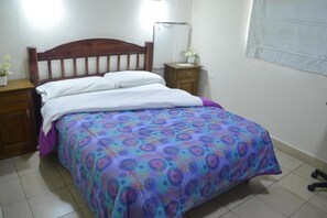 A bedroom with a wooden headboard, a bed with a patterned bedspread, a nightstand with a lamp, and a window with a curtain. - Hosteria San Benito (Concordia)