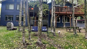 A two-story house with a deck, surrounded by trees and a grassy yard. - Your Cozy Anchorage Retreat (Anchorage)