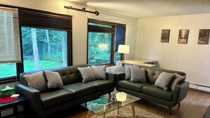 A living room with two dark sofas, a glass coffee table, a patterned rug, and a desk with a lamp. - Your Cozy Anchorage Retreat (Anchorage)