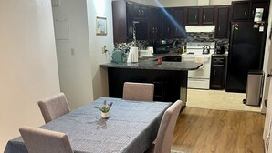 A modern kitchen with dark cabinets, a central island, and a dining area with a table and chairs. - Your Cozy Anchorage Retreat (Anchorage)