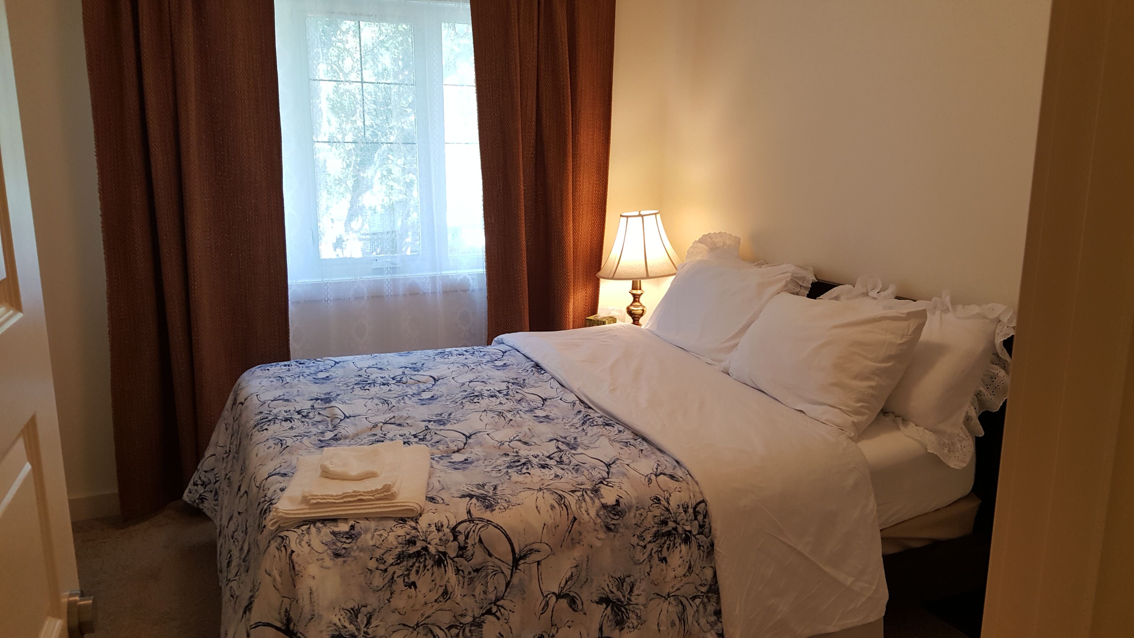 A neatly made bed with a floral bedspread, a bedside lamp, and a window with curtains.