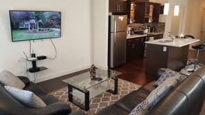 A modern living room with a glass coffee table, leather sofa, and a TV mounted on the wall. - Modern Vacation Home Near West Edmonton Mall, Transit Center & LRT - 3BR (Edmonton)