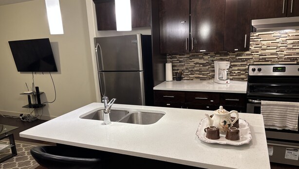 A modern kitchen with dark wooden cabinets, stainless steel appliances, a white speckled countertop, and a built-in oven. - Modern Vacation Home Near West Edmonton Mall, Transit Center & LRT - 3BR (Edmonton)