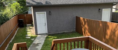 A wooden deck with a table and chairs, a grassy yard, and a house in the background.