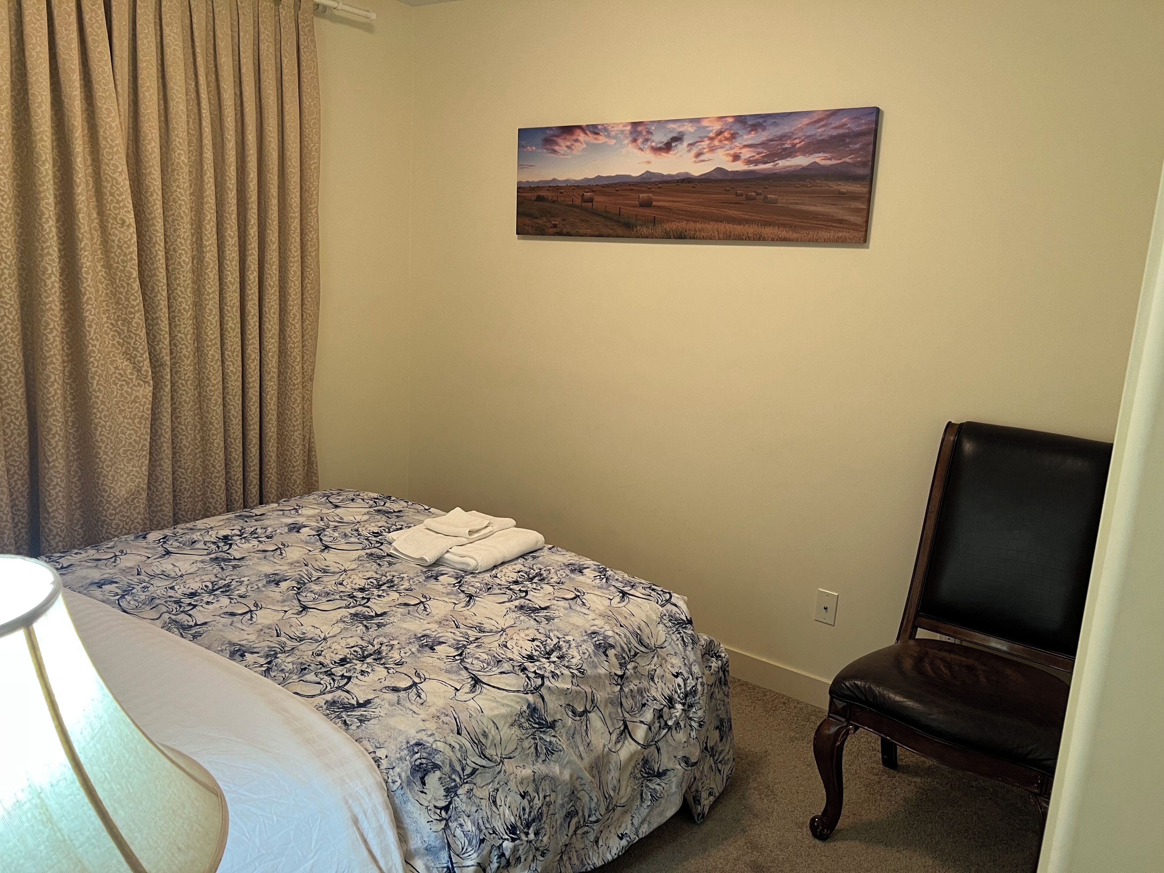 A bedroom with a bed, a chair, a painting, and a curtain.