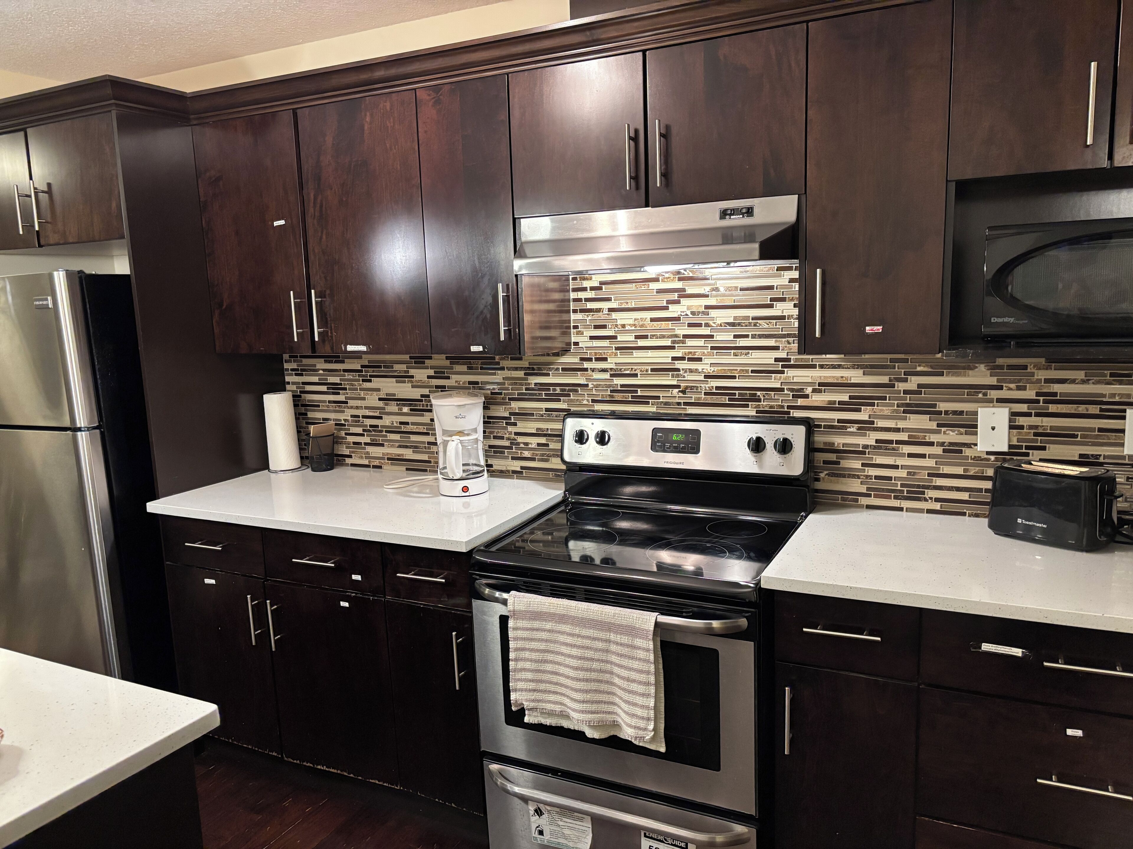 A kitchen with dark wood cabinets, stainless steel appliances, and a tiled backsplash.