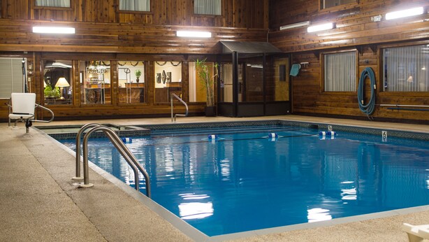Piscina interior con paredes de madera, una escalera de piscina y agua azul cristalina.