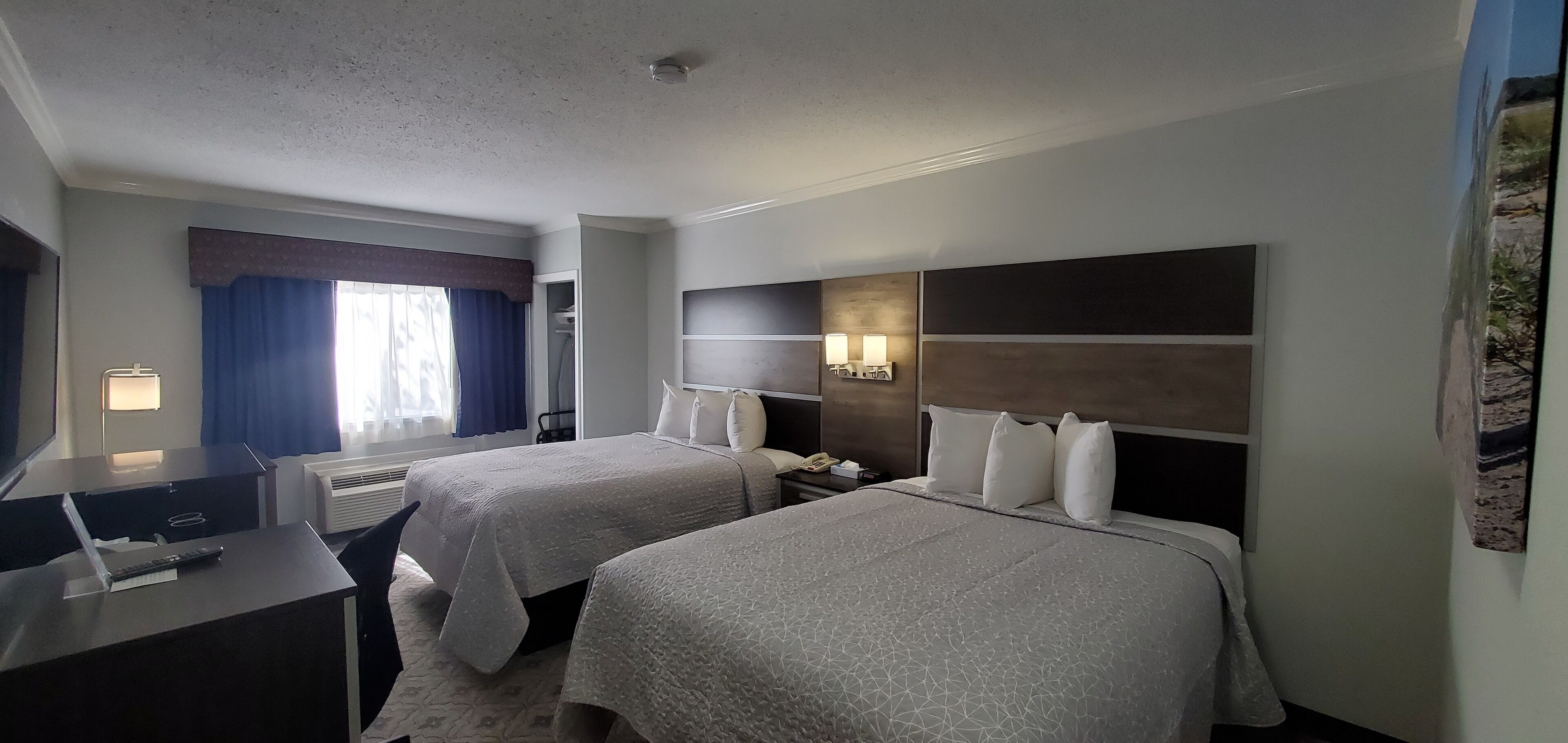 Ein Hotelzimmer mit zwei Betten, einem Schreibtisch, einem Stuhl, einer Schreibtischlampe, einem Telefon und einer Wandleuchte.