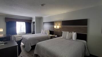 Ein Hotelzimmer mit zwei Betten, einem Schreibtisch, einem Stuhl, einer Schreibtischlampe, einem Telefon und einer Wandleuchte.