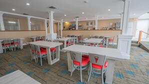 Un comedor amplio con varias mesas y sillas, una barra con caja registradora y una alfombra estampada.