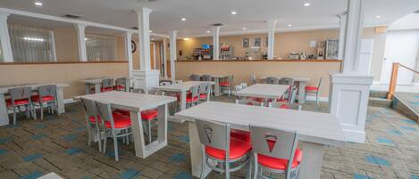 A spacious dining area with multiple tables and chairs, a counter with a cash register, and a patterned carpet.
