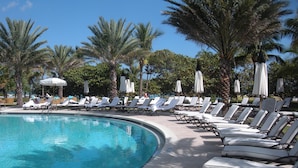 A pool area with sun loungers and umbrellas, surrounded by palm trees. - One Bal Harbour Hotel and Resort, Deluxe 2 bedroom private unit @ the Ritz (Bal Harbour)