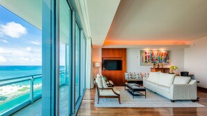 A spacious living room with a large window overlooking the ocean, a white sofa, a wooden coffee table, and a flat-screen TV mounted on the wall. - One Bal Harbour Hotel and Resort, Deluxe 2 bedroom private unit @ the Ritz (Bal Harbour)