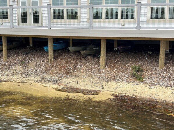 A waterfront property with a wooden deck, boats, and a sandy shoreline.