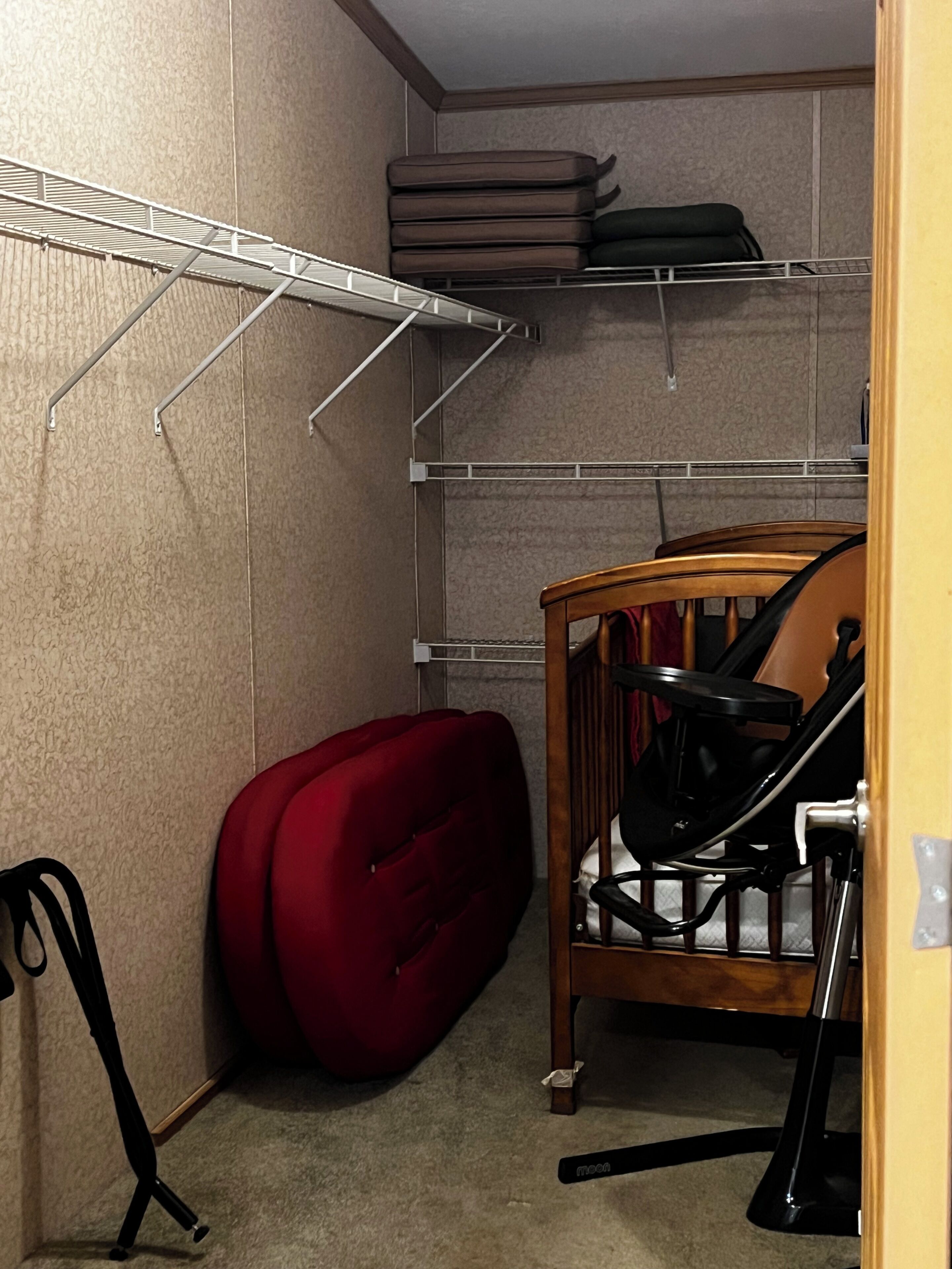 Une petite pièce comprenant un berceau, une chaise rouge et une étagère en métal.