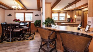 Una cocina con vigas de madera, una zona de comedor con mesa y sillas, y una barra con taburetes.