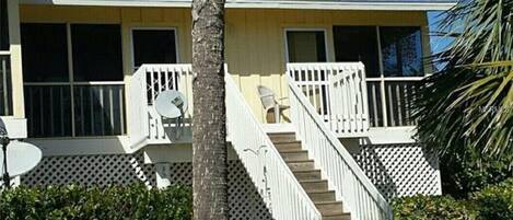 A two-story house with a white exterior, a front porch with a white railing, and a staircase leading to the second floor.