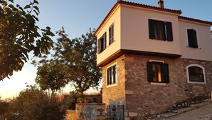 Una casa de piedra de dos pisos, con fachada de piedra, un balcón y un pequeño jardín.