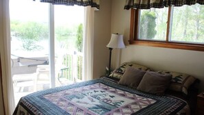 A bedroom with a large bed, a window with curtains, a nightstand, and a lamp. - Quietwater Cottage-On Water/Nature/Hiking/Relaxing/ Hot Tub & Sauna, Peaceful! (Poynette)