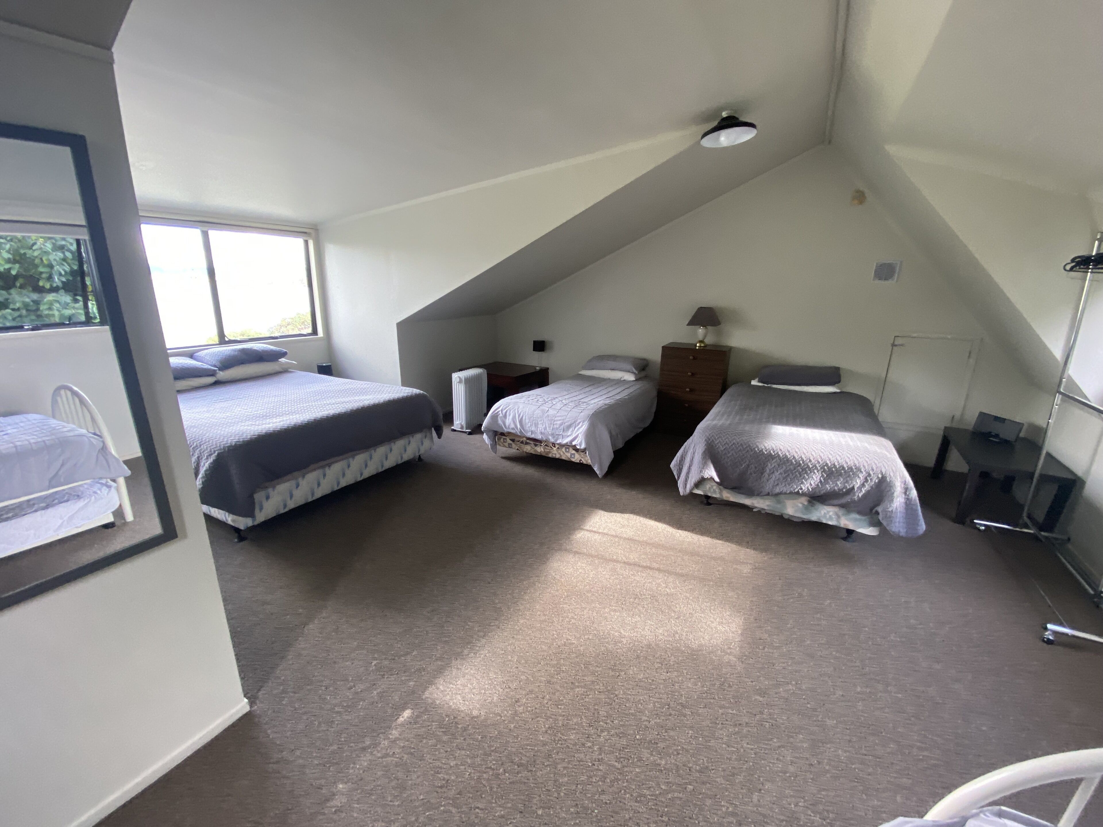 A room with two beds, a radiator, a desk, and a lamp.