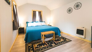 Un dormitorio con cama, mesitas de noche, un calentador, una ventana con cortinas y un estante fijado a la pared.