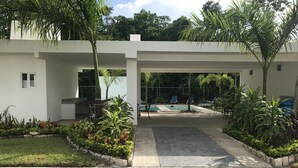Un edificio moderno con área de piscina, rodeado de abundante vegetación y palmeras.