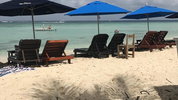 Una playa con sillas y sombrillas de playa, una vista despejada del océano y un barco a lo lejos.