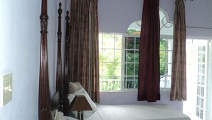 Una camera da letto con un letto a baldacchino, una finestra con tende e vista su del verde all'esterno.