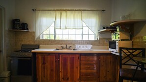 Una cucina con mobili in legno, un fornello, un forno a microonde e una finestra con tende.