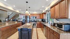Una cocina amplia con encimeras de granito, armarios de madera y electrodomésticos de acero inoxidable, e una isla central.