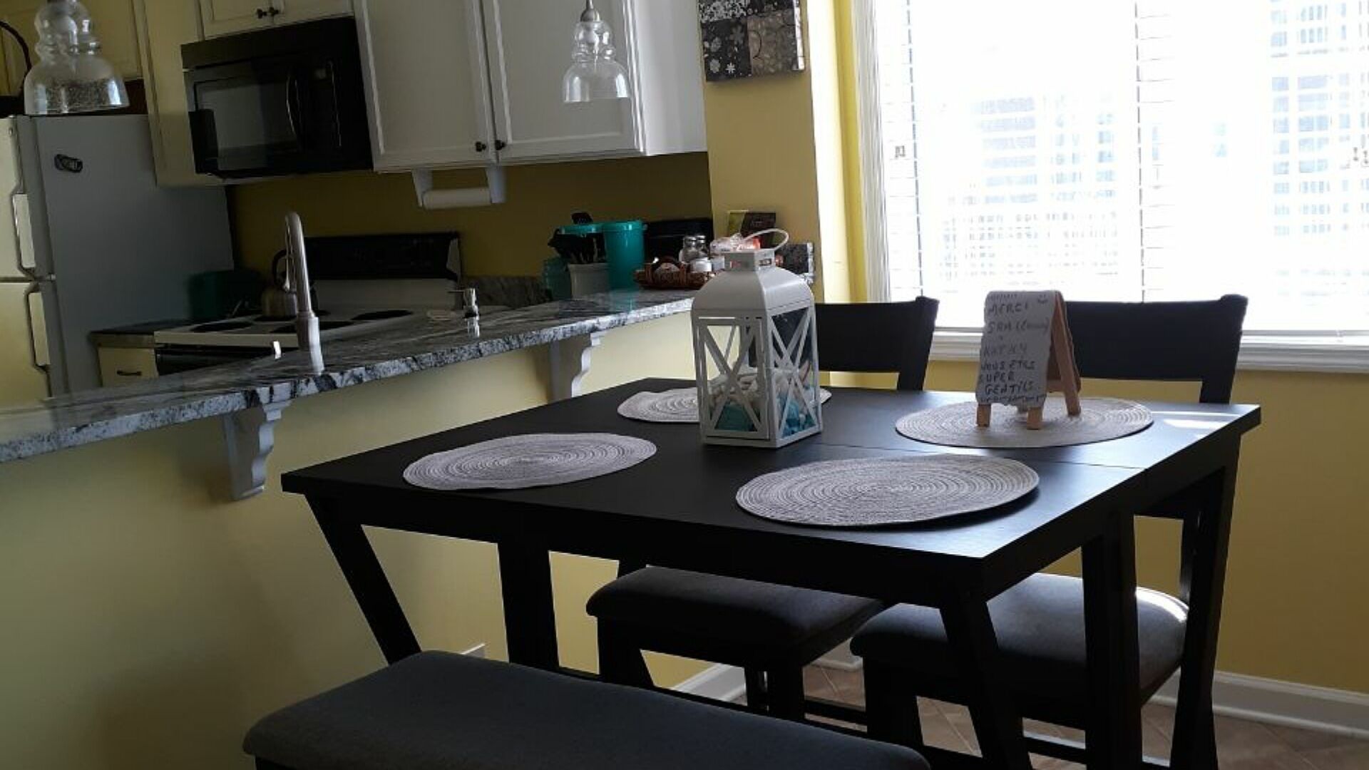 A dining area with a black table, white placemats, and a lantern.