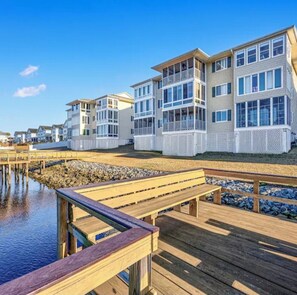 A coastal residential area with multi-story houses, wooden walkways, and a dock extending into the water.