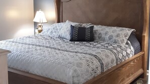 Ein Schlafzimmer mit einem hölzernen Bett, gemusterten Betttextilien, einer Nachttischlampe und einem gerahmten Bild an der Wand.