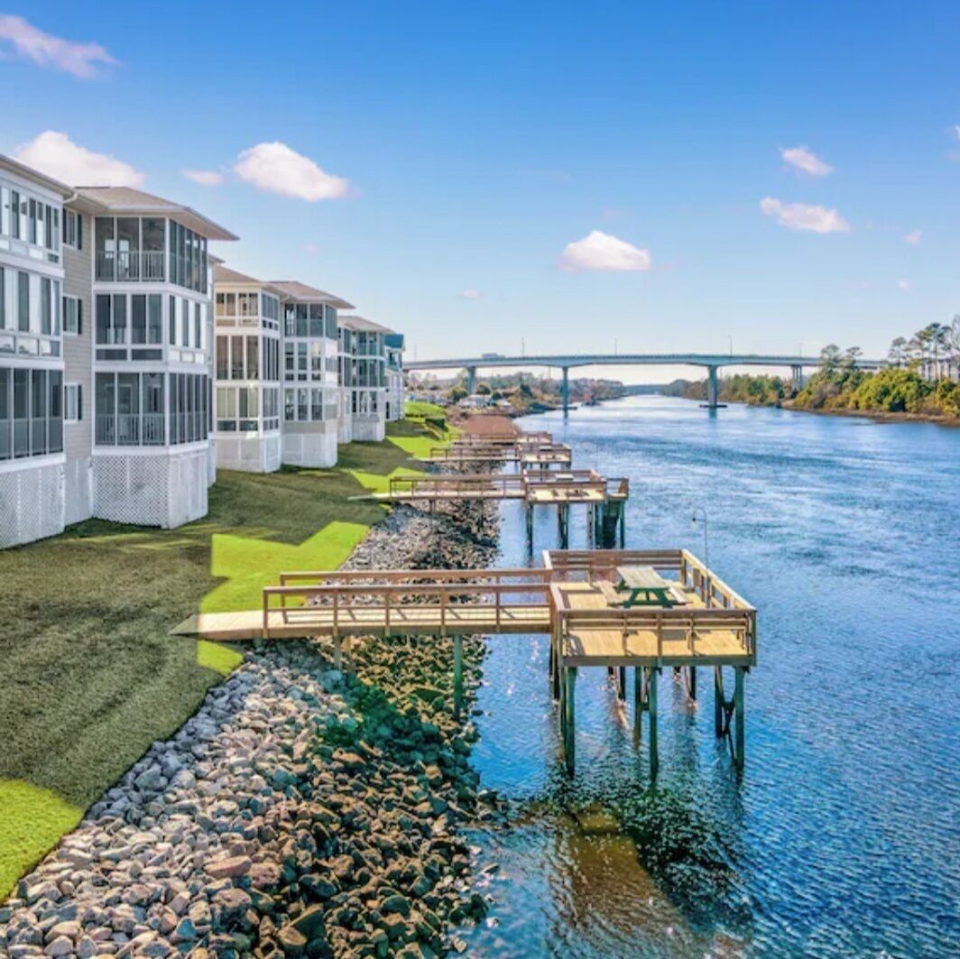 Une propriété située au bord de l’eau, dotée d’une architecture moderne, avec une rivière et un pont en arrière-plan.